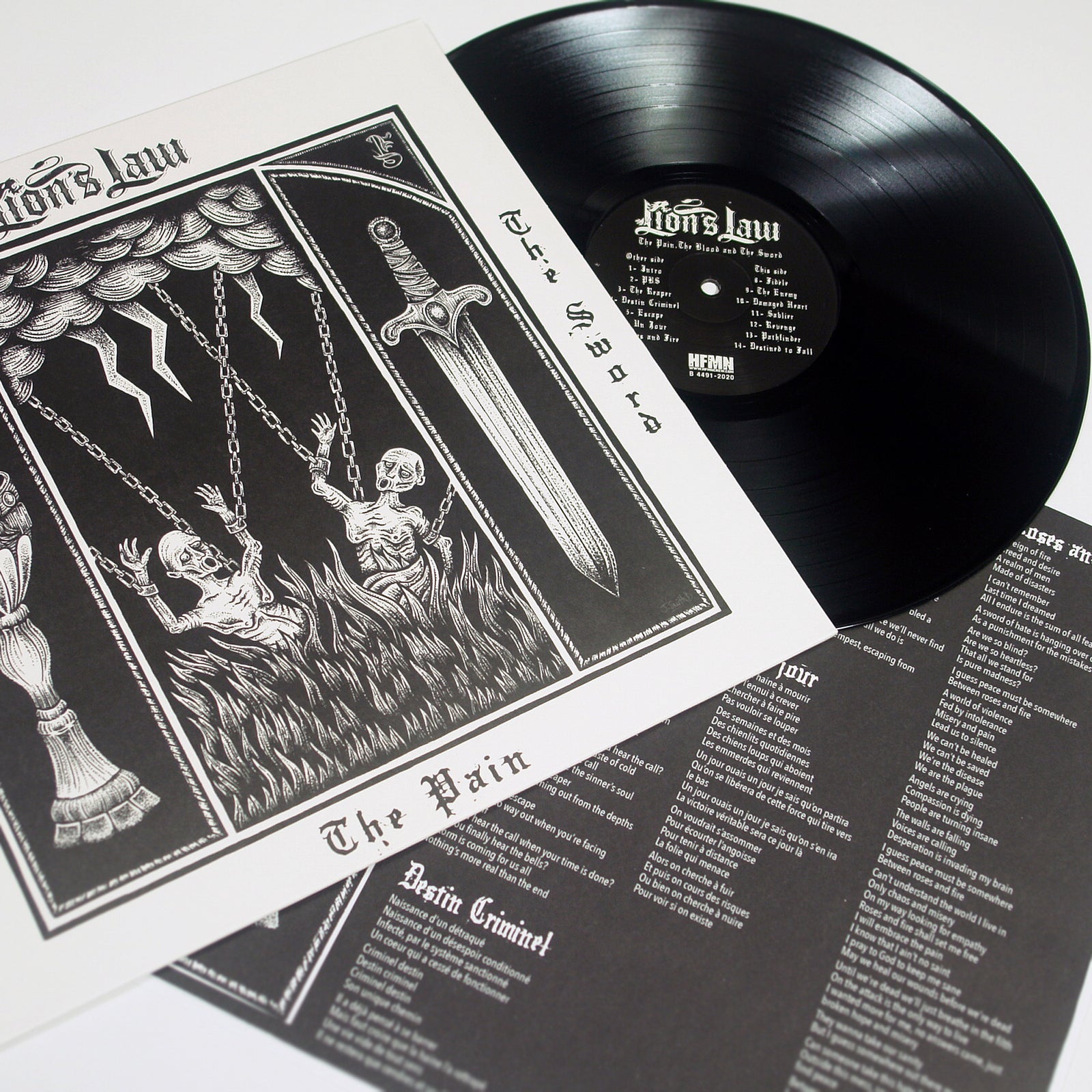 A black Lions Law vinyl record is partially out of its sleeve. The cover art features two skeletons on swings under stormy clouds with lightning and a sword, evoking the hardcore scene. A lyrics sheet lies beside the record.