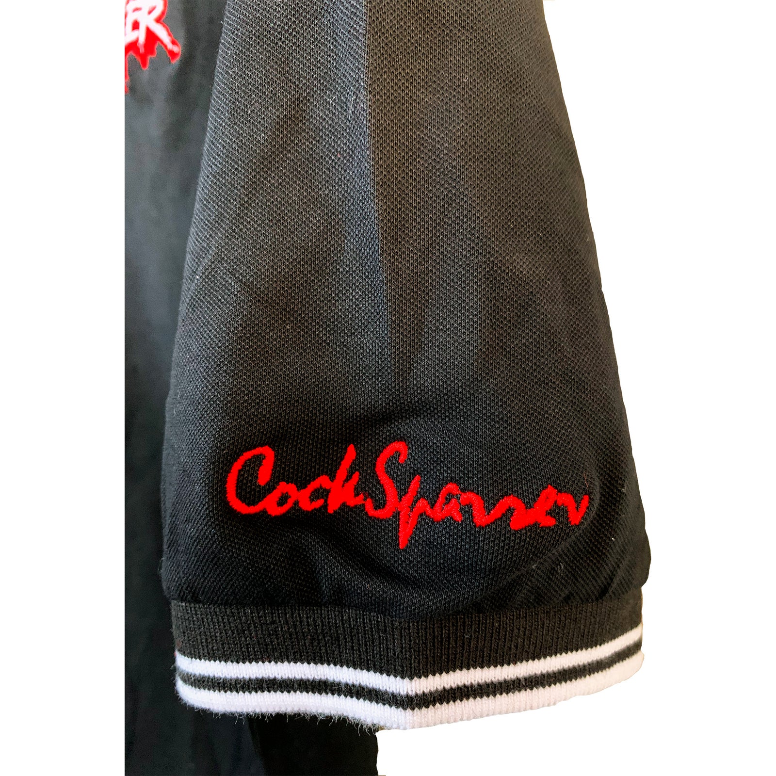 A black jacket sleeve with a white-striped cuff and Cock Sparrer embroidered in bright red cursive is perfect for fans of the Cock Sparrer brand or anyone who appreciates classic polo and embroidered crest styles.