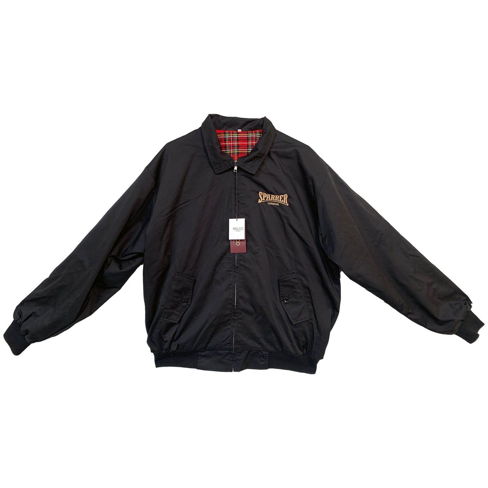 A black Cock Sparrer Harrington jacket with a collar, buttoned cuffs, and red plaid lining. Features a front zipper, two pockets, Cock Sparrer logo on the left chest, and a tag attached to the zipper pull.