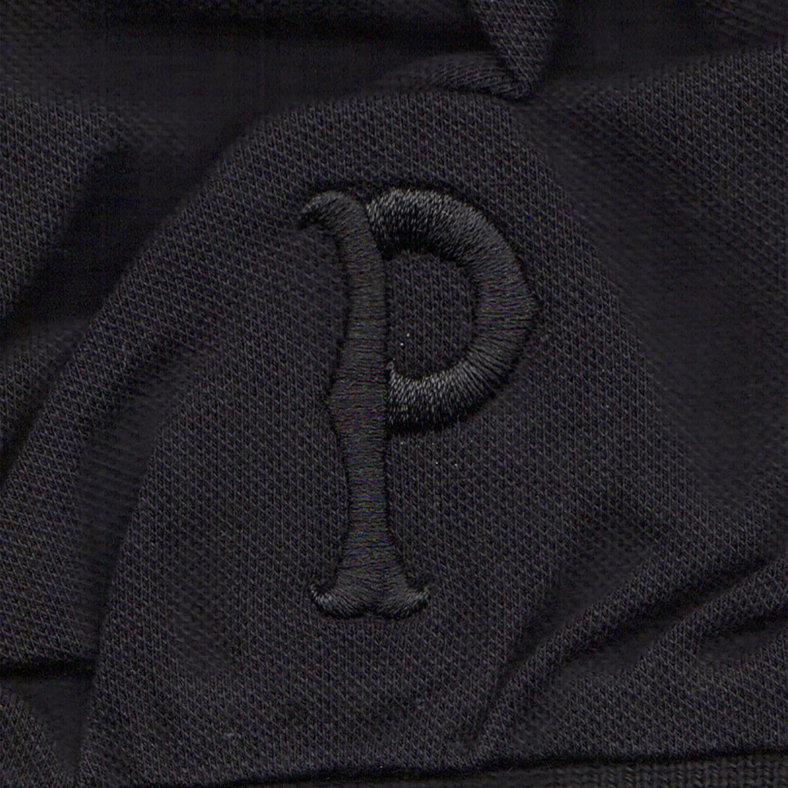 A black polo with a textured finish features a raised, embroidered letter P in black thread—ideal for fans of Pirates Press Records.