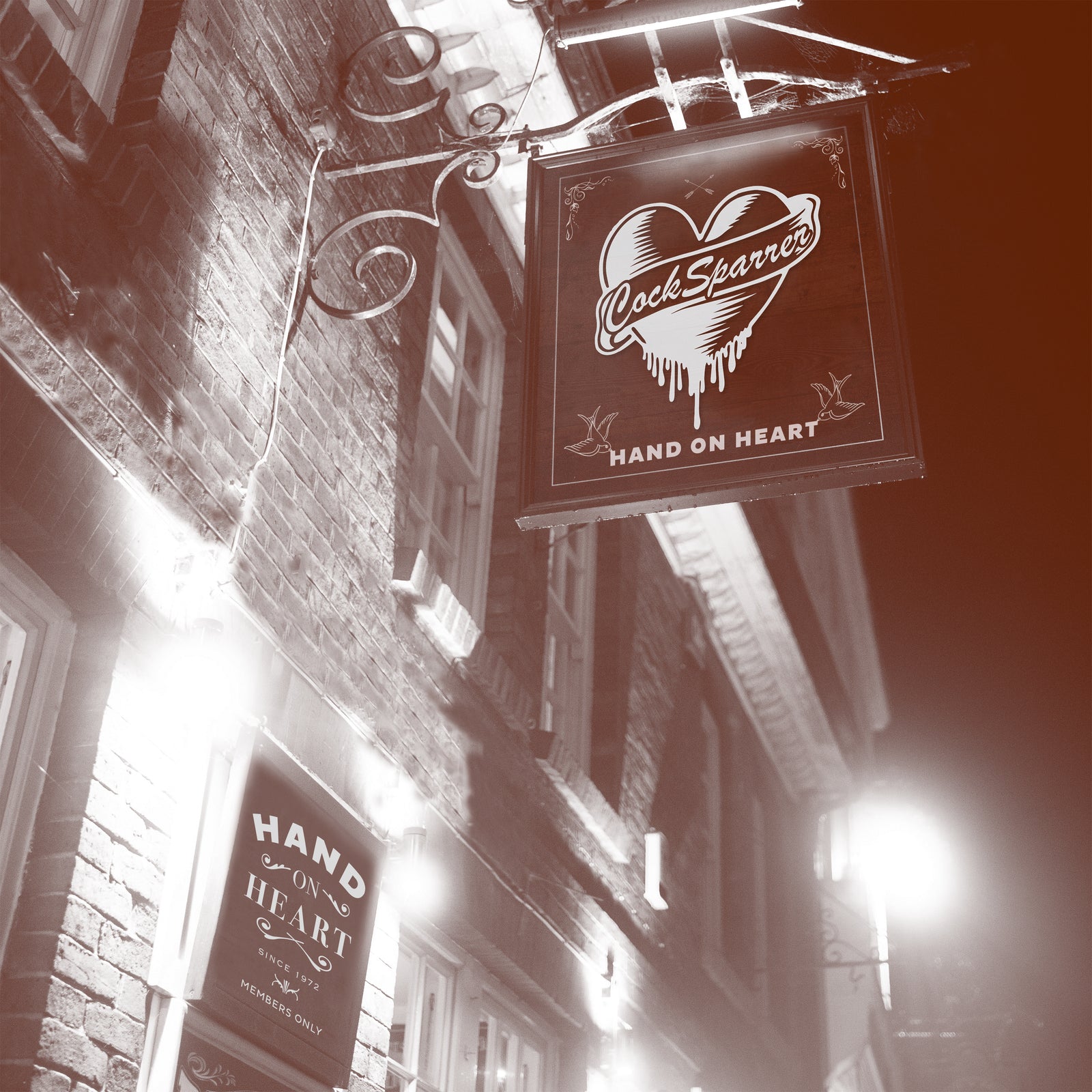 Sepia photo of a brick building at night, featuring Cock Sparrer’s heart-shaped sign lit up with Hand On Heart below—classic punk rock mood. Another painted wall sign reads Hand On Heart and Members Only. Brand: Cock Sparrer.