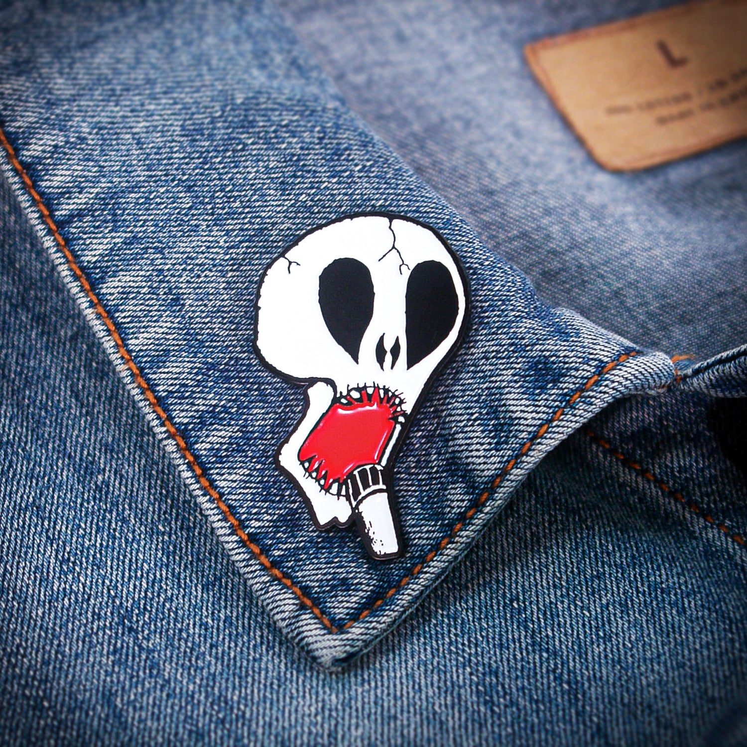 A Subhumans denim jacket featuring a collar pin of a white cracked skull with black eye sockets, biting a red popsicle.