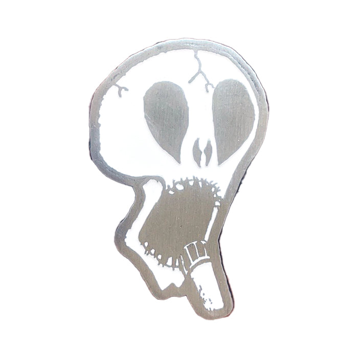 A Subhumans silver enamel pin shaped like a skull, with large dark eye sockets and a jagged mouth holding a cigarette, set against a white background.