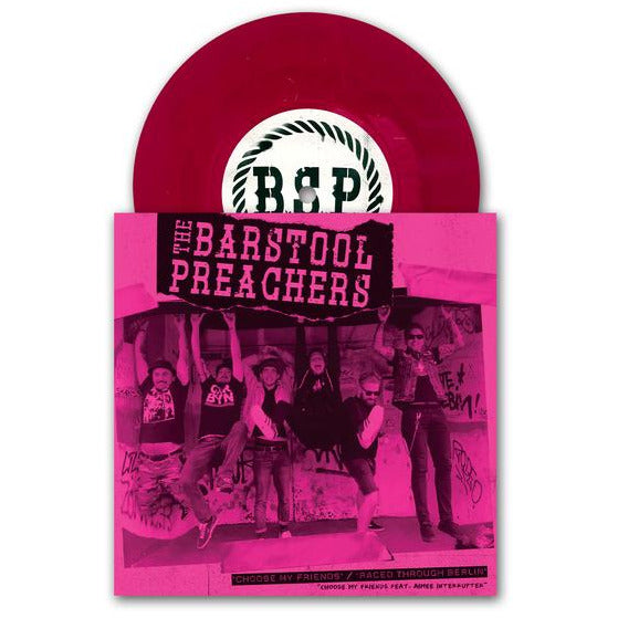 A hot pink vinyl record partially in its sleeve, which displays a bold pink photo of The Bar Stool Preachers posing by a graffiti wall, their name in block letters above, and Choose My Friends featured on the cover.