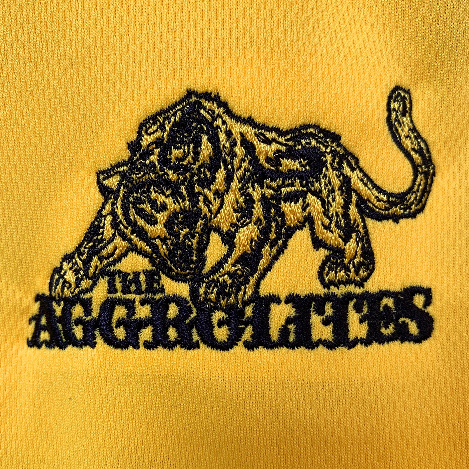 Embroidered The Aggrolites prowling tiger logo with black outline on yellow fabric. The bold design stands out and is perfect for any Aggrolites soccer jersey or REGGAE NOW! 20 collection. Brand: The Aggrolites.