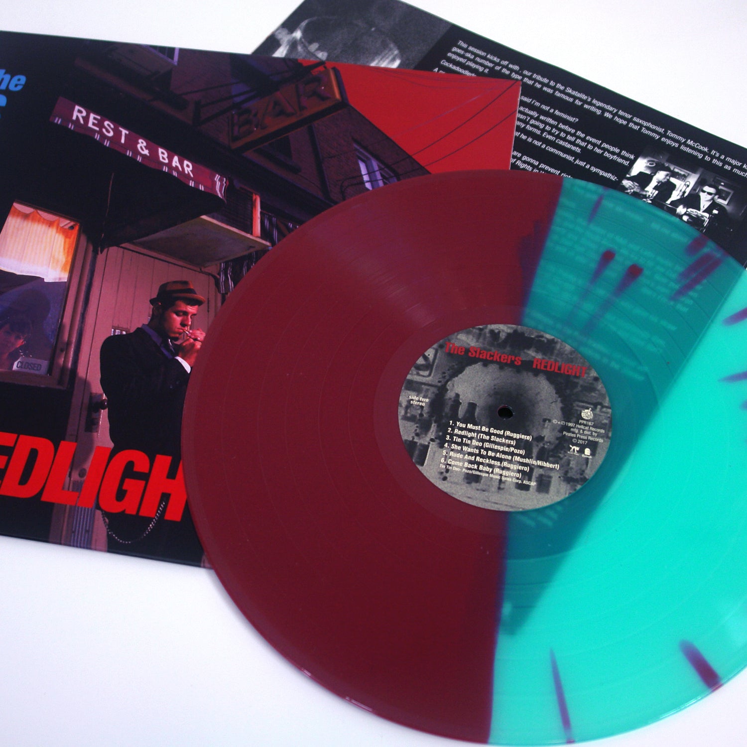 A maroon and teal split vinyl by The Slackers rests on its album cover, which shows a suited man in a hat outside a bar. Liner notes appear in the background, evoking classic ska band vibes.
