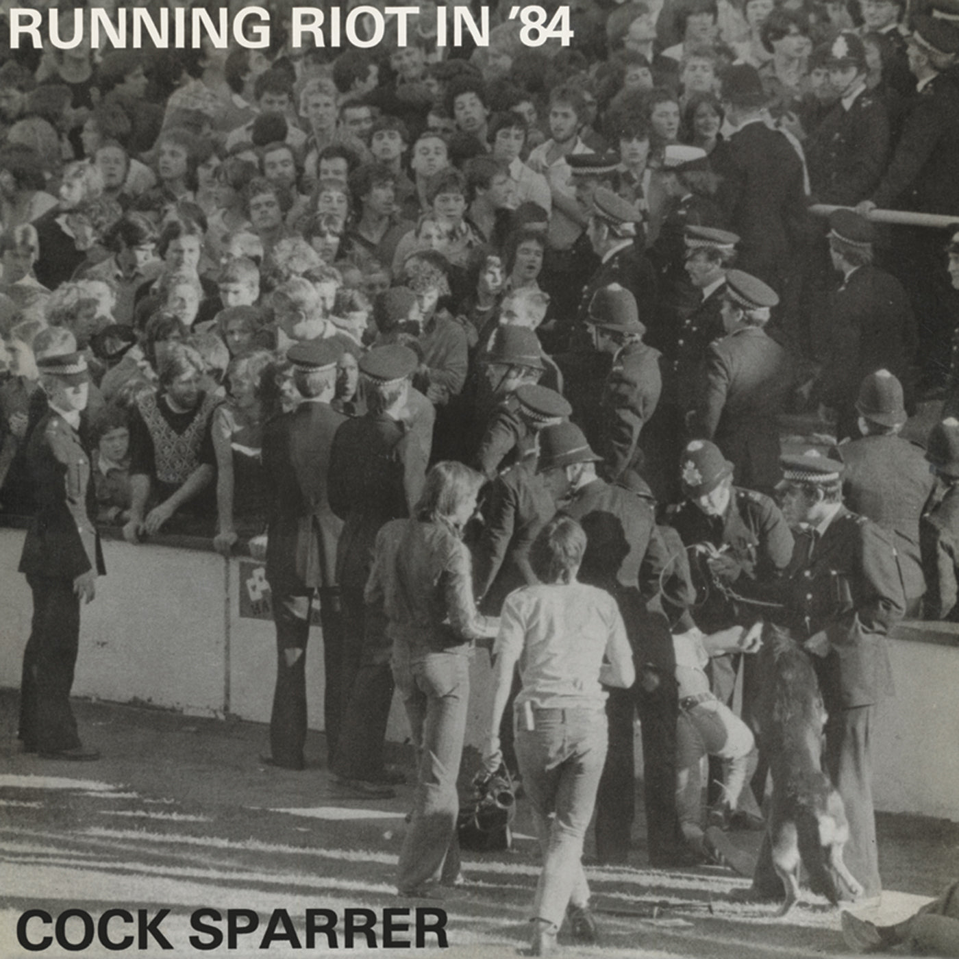 Black-and-white photo shows police and a dog facing stadium fans, with RUNNING RIOT IN ’84 at the top and Cock Sparrer 50th anniversary at the bottom. Brand: Cock Sparrer.