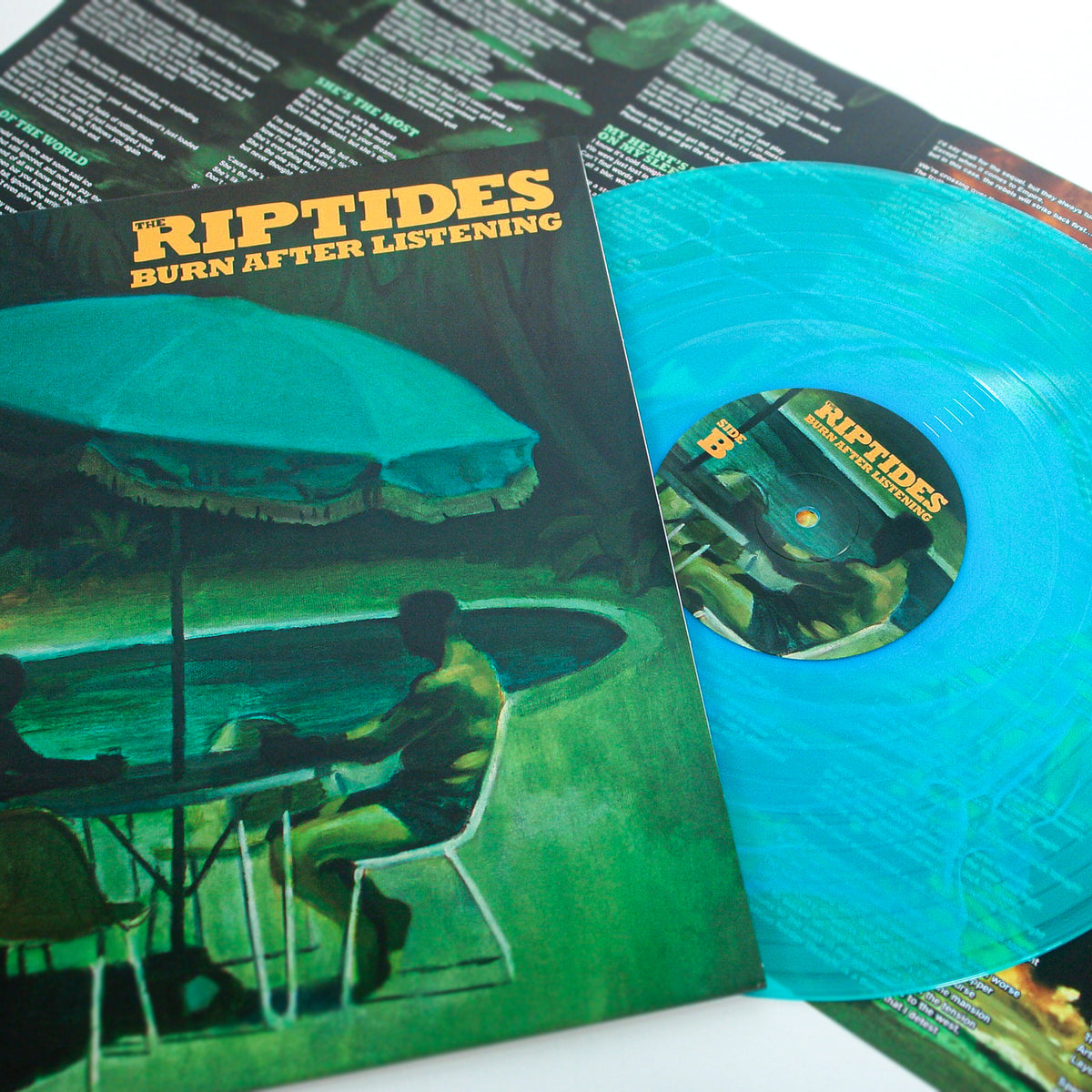 A turquoise Vinyl LP and cover feature a person by a pool under an umbrella. The Riptides’ album &quot;Burn After Listening&quot; includes an open lyric sheet in the background.