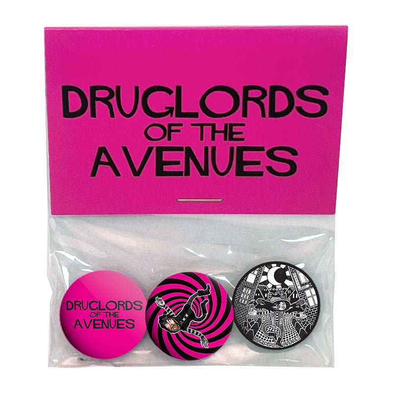 A set of three collectible buttons by Druglords of The Avenues comes in a clear bag with a bright pink label. Each button showcases unique colorful and black-and-white designs—ideal for fans and collectors alike.