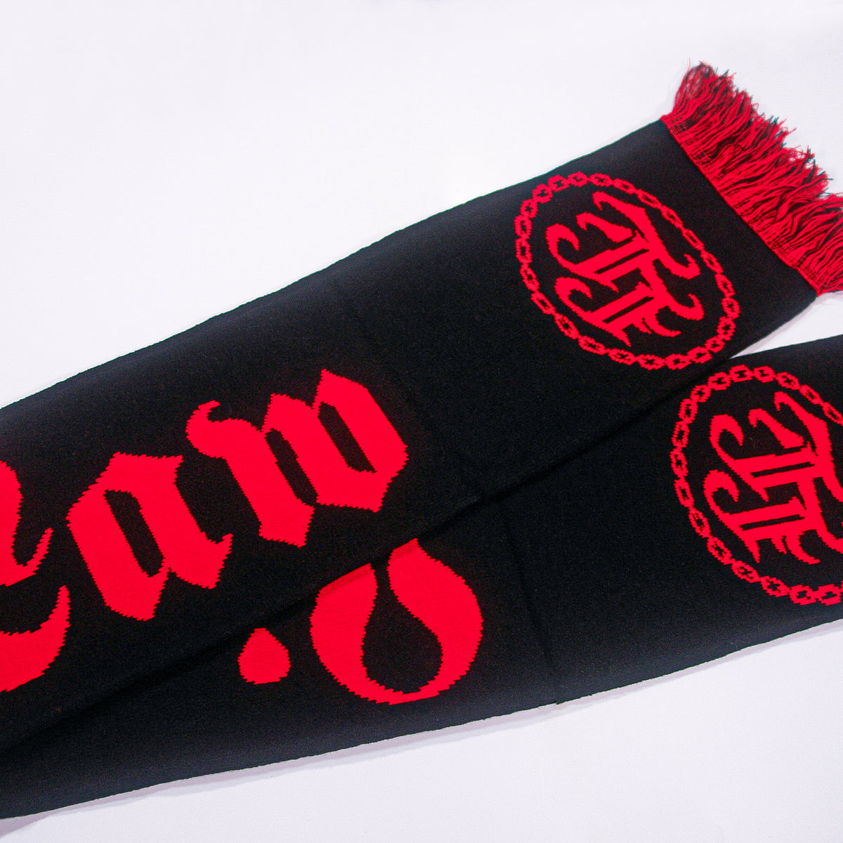 A bold black scarf by Lion&#39;s Law featuring their logo in red Gothic-style text and circular emblems, plus decorative fringes at one end—an eye-catching band accessory shown on a white background.