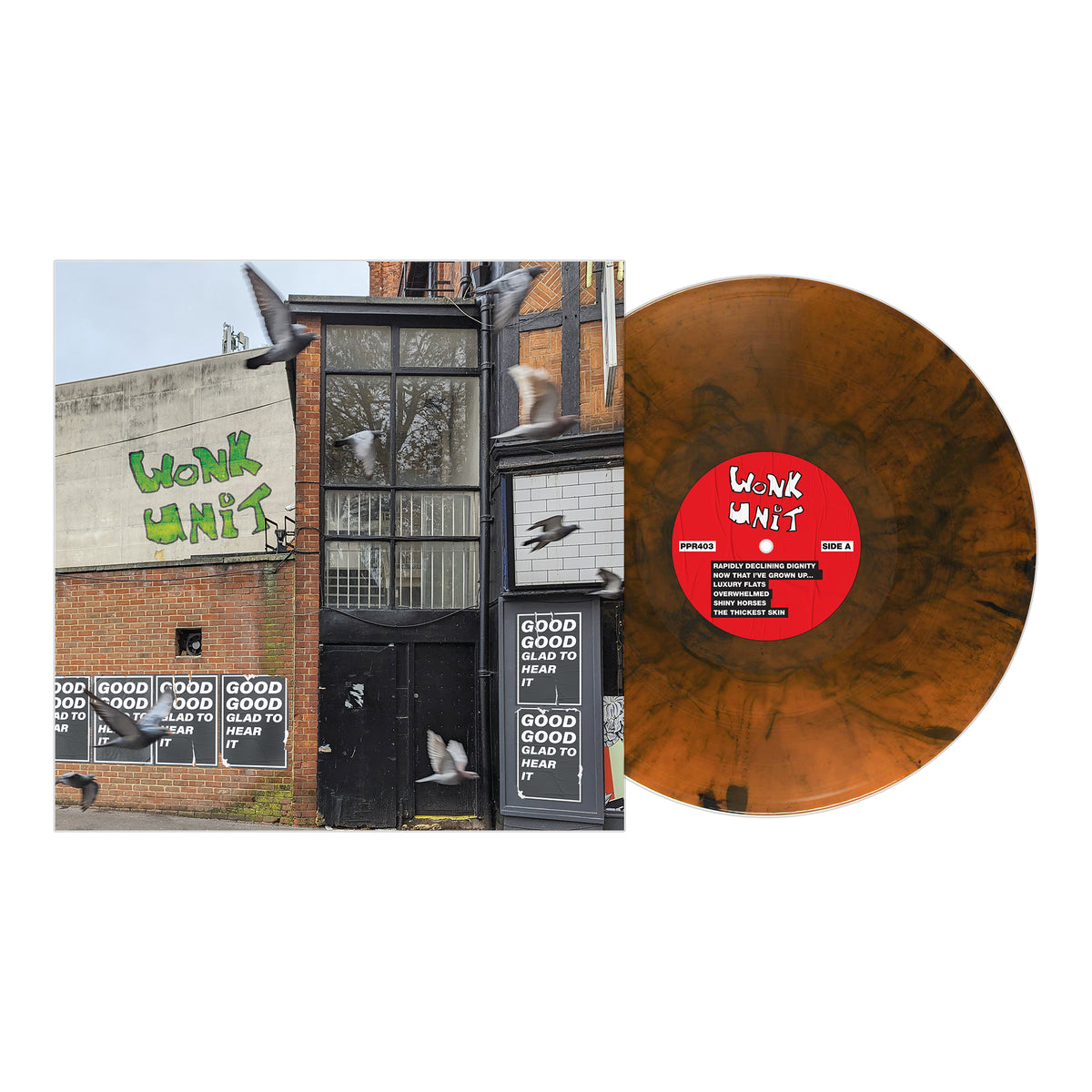 A brown and black marbled vinyl from Wonk Unit sits next to an album cover showing a graffiti-tagged brick building, Good Good Glad To Hear It posters in the windows, and pigeons flying past.
