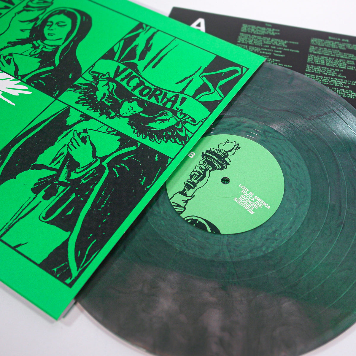 A Downtown Struts vinyl record with a green label sits in its illustrated green and black sleeve showing a statue, hand with book, "VICTORIA!" above a wreath, and is accompanied by the lyrics sheet for their punk rock track "Sail the Seas Dry.