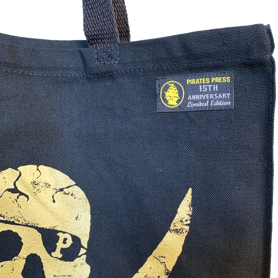 A close-up of an anniversary canvas bag from Pirates Press Records shows part of a gold skull and crossbones. A small tag reads PIRATES PRESS 15TH ANNIVERSARY Limited Edition, with a yellow logo above the text.