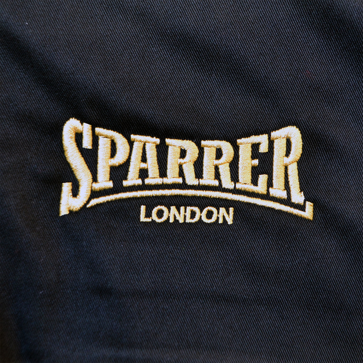 Embroidered text on dark fabric reads Cock Sparrer London in bold letters, with light stitching that stands out against the background, channeling the classic Cock Sparrer style seen on a Harrington jacket.