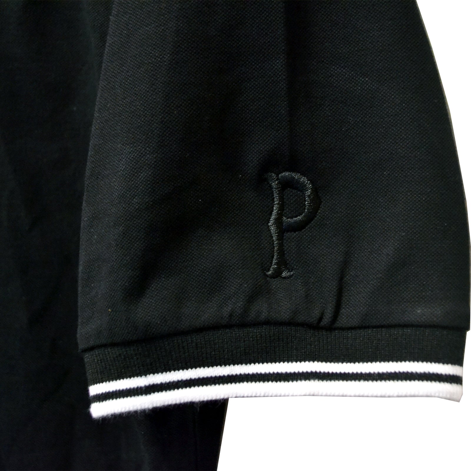 A close-up of a black Pirates Press Records polo featuring white and black striped cuffs and an embroidered letter P on the sleeve, inspired by their iconic One Family One Flag design.