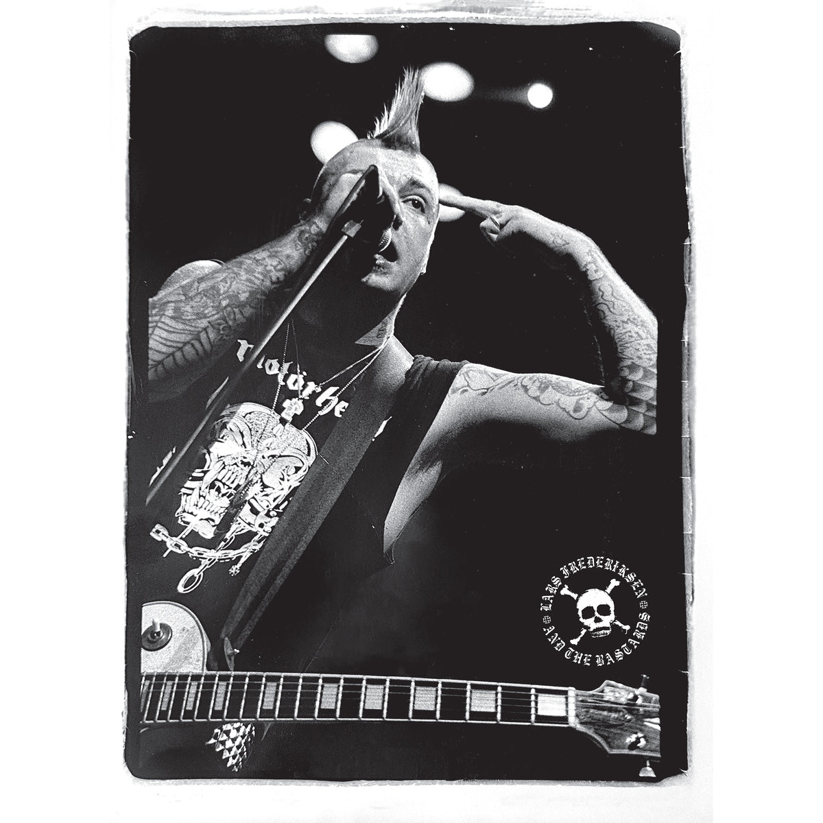 Black and white photo of a tattooed musician with a mohawk singing into a microphone while playing electric guitar, pointing to their head. The circular skull logo is on the bottom right, referencing Lars Frederiksen and The Bastards’ self-titled debut album, now available on colored vinyl.