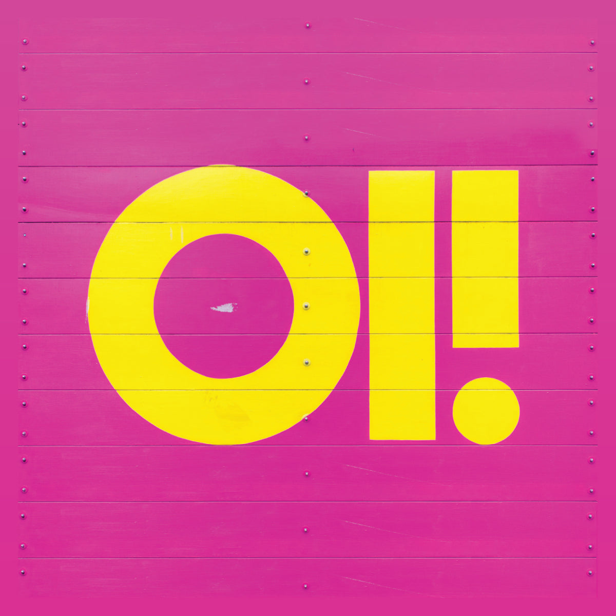 Bold yellow “OI!” in playful full-color sticker style pops against a pink wooden wall with visible lines and bolts, creating a vibrant contrast—showcasing Pirates Press Records’ eye-catching design.