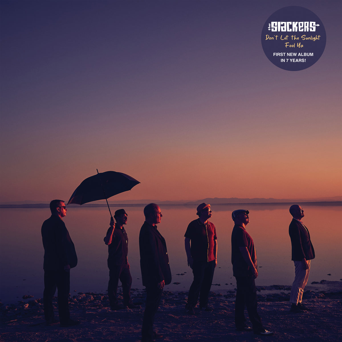 Five people in silhouette stand by a calm lakeshore at sunset, one holding an umbrella. Deep orange and purple hues glow as The Slackers’ album text reads: Don’t Let the Sunlight Fool Ya. Brand Name: The Slackers.