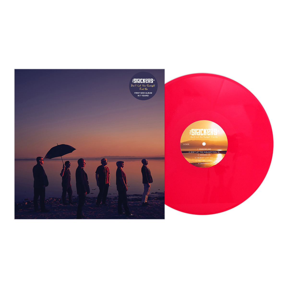 A red vinyl record beside its album cover, showing The Slackers by the water at sunset—one holds an umbrella. The album, Don’t Let The Sunlight Fool Ya, is from brand The Slackers.