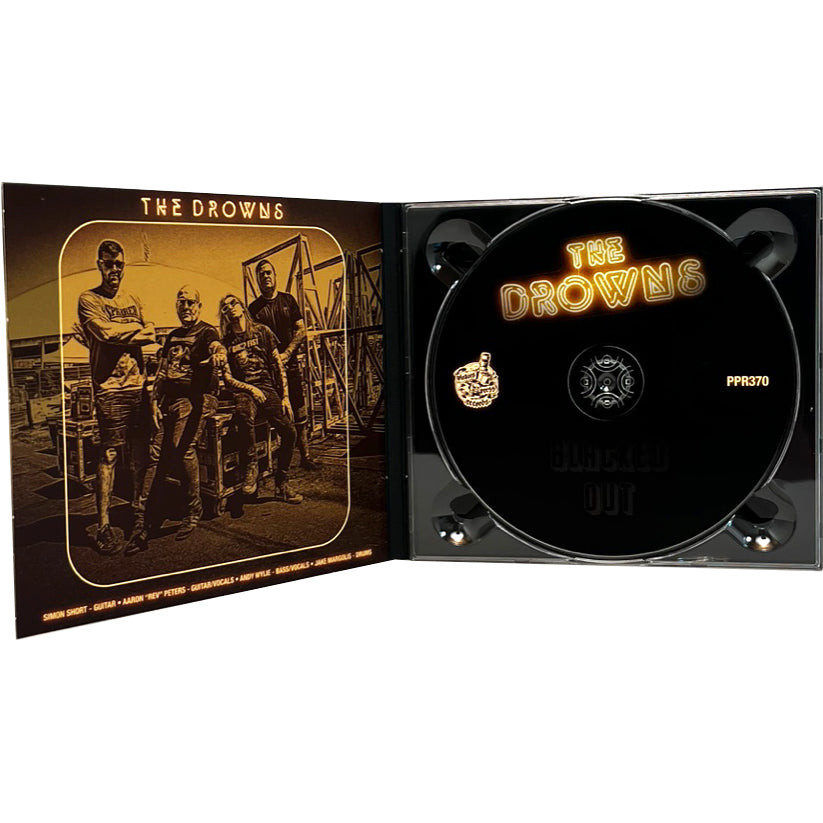 An open CD case for The Drowns shows a sepia-toned photo of the four band members on the left and a CD with The Drowns name and yellow logo on a black background on the right.