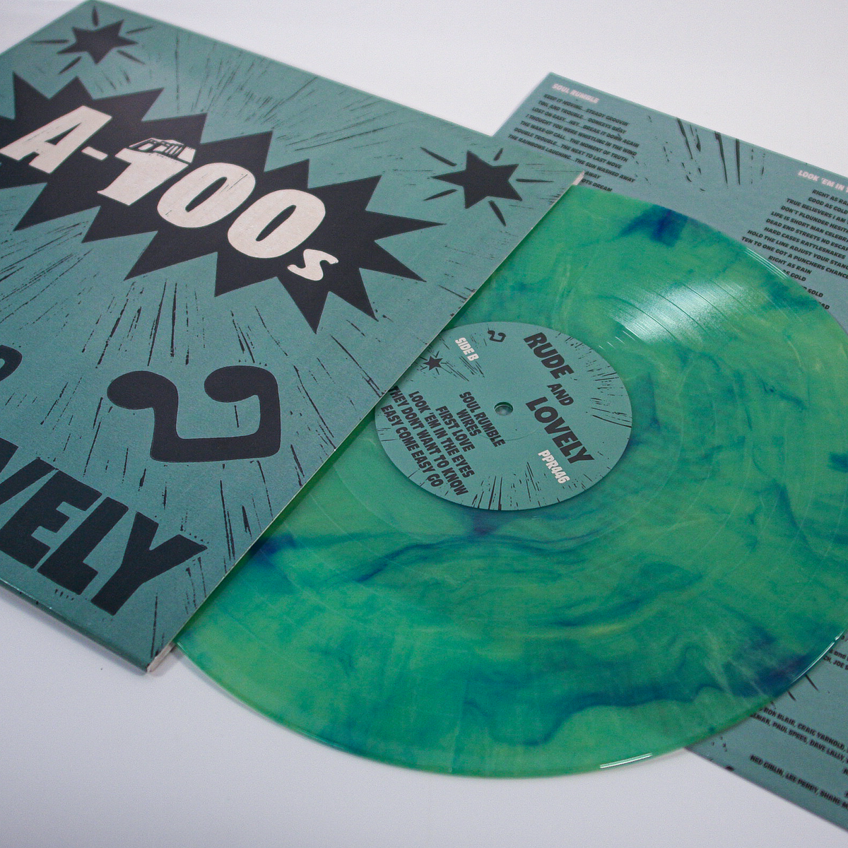 A green and blue marbled A-100s vinyl record, ideal for reggae and ska fans, is partly out of its teal cover with a song lyrics sheet beside it for an enhanced listening experience.