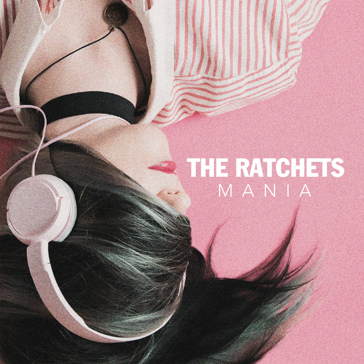A person with dark hair wearing headphones lies on a pink surface next to The Ratchets Mania text.