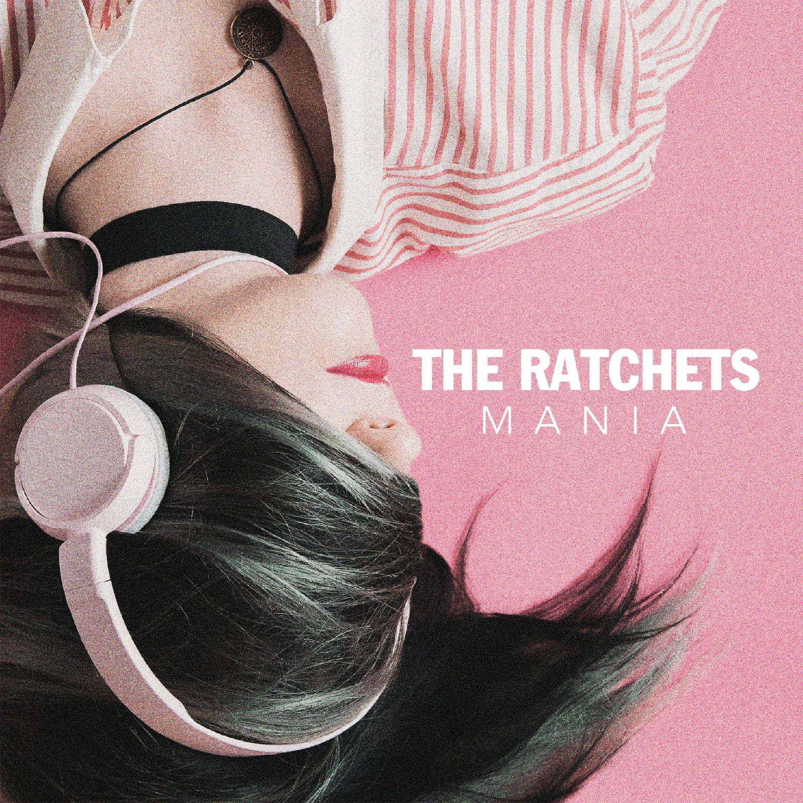 A person with dark hair wearing headphones lies on a pink surface next to The Ratchets Mania text.