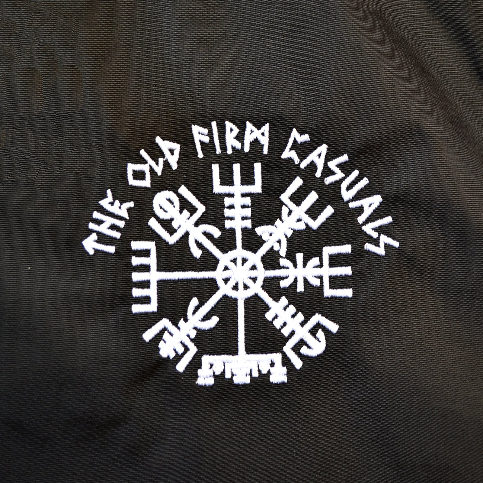 A black windbreaker from The Old Firm Casuals, featuring a white embroidered Vegvisir symbol with THE OLD FIRM CASUALS in a curved, stylized font above it.