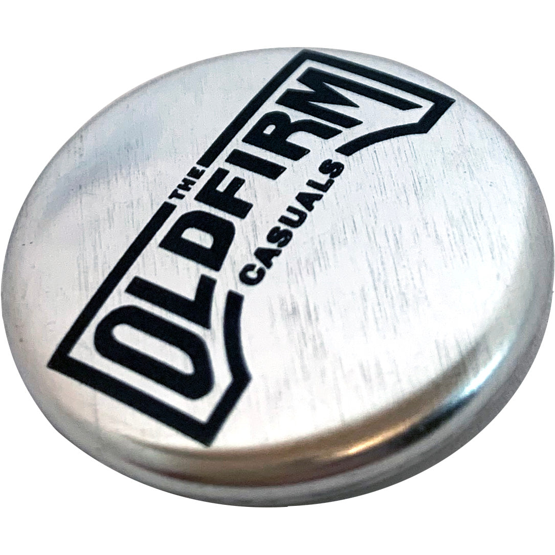 A round metallic silver button displaying &quot;The Old Firm Casuals&quot; brand name in bold black letters on a sleek silver background.
