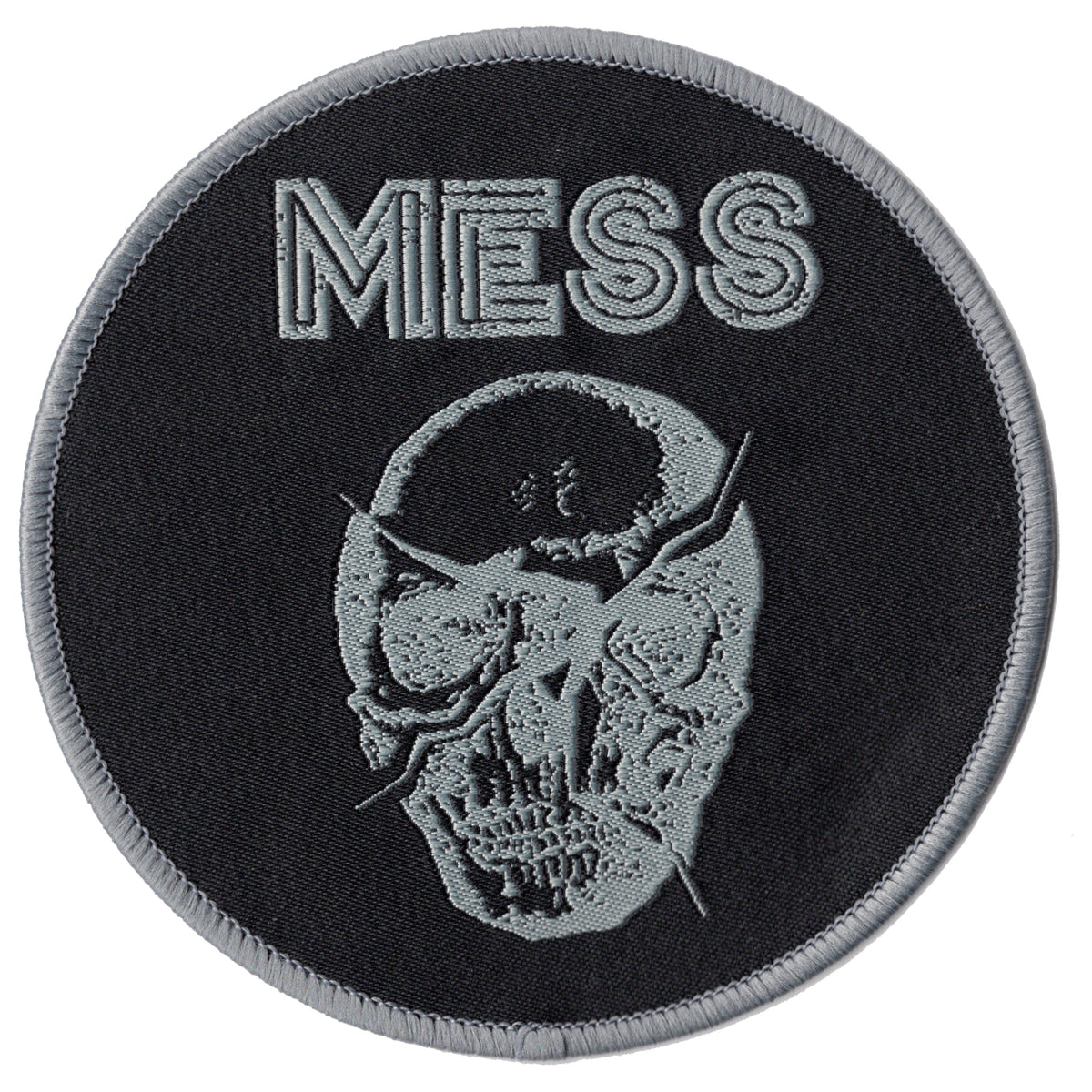 This circular woven patch by Mess features MESS at the top and a cracked skull logo below, both finely embroidered in light gray on a black background with a subtle gray border.