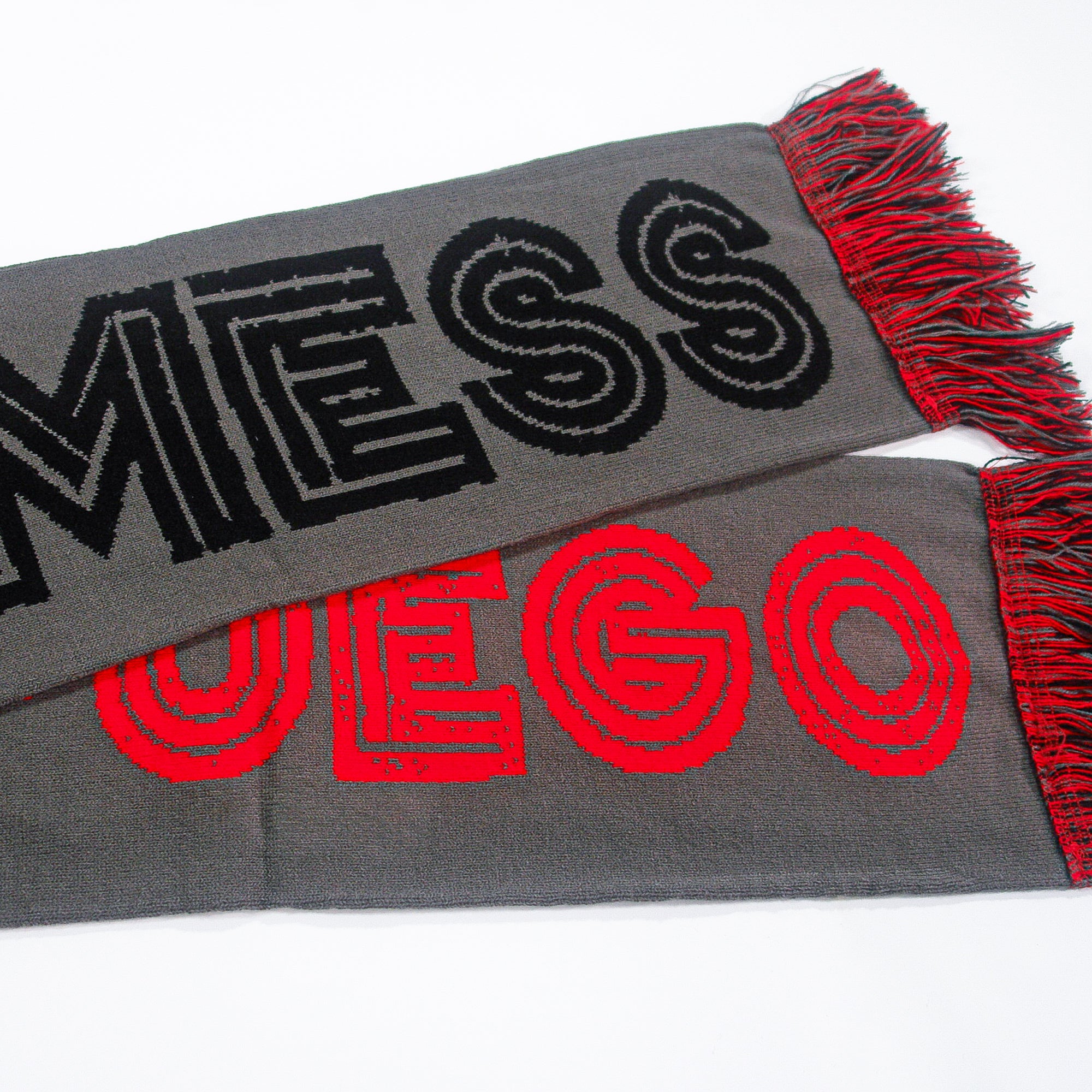 A sleek gray scarf by Mess with bold black "MESSI" and red "FUEGO" text, plus red and black fringe.