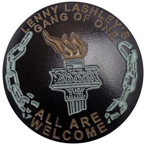 This round enamel pin features a torch and broken chains, with &quot;Lenny Lashley&#39;s Gang Of One&quot; at the top and &quot;All Are Welcome&quot; at the bottom—an ideal accessory for any fan of Lenny Lashley&#39;s Gang Of One.