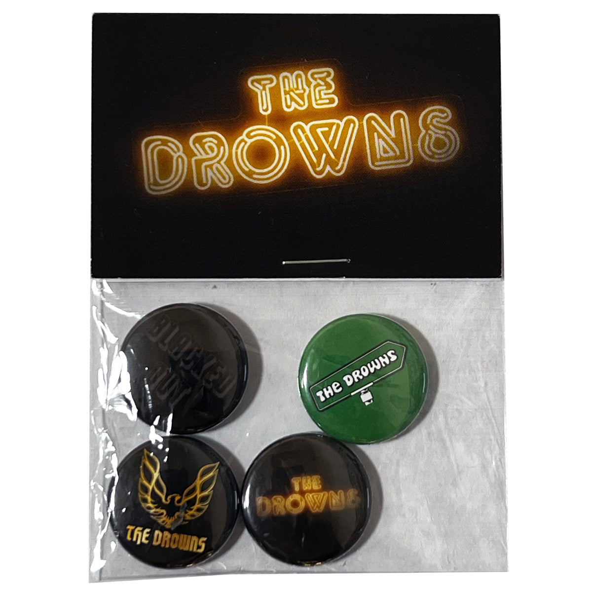 A set of four The Drowns band buttons in a plastic bag, displayed on a hang card with The Drowns in yellow neon-style text. Includes assorted designs such as blacked-out buttons and classic band logos. Brand: The Drowns.
