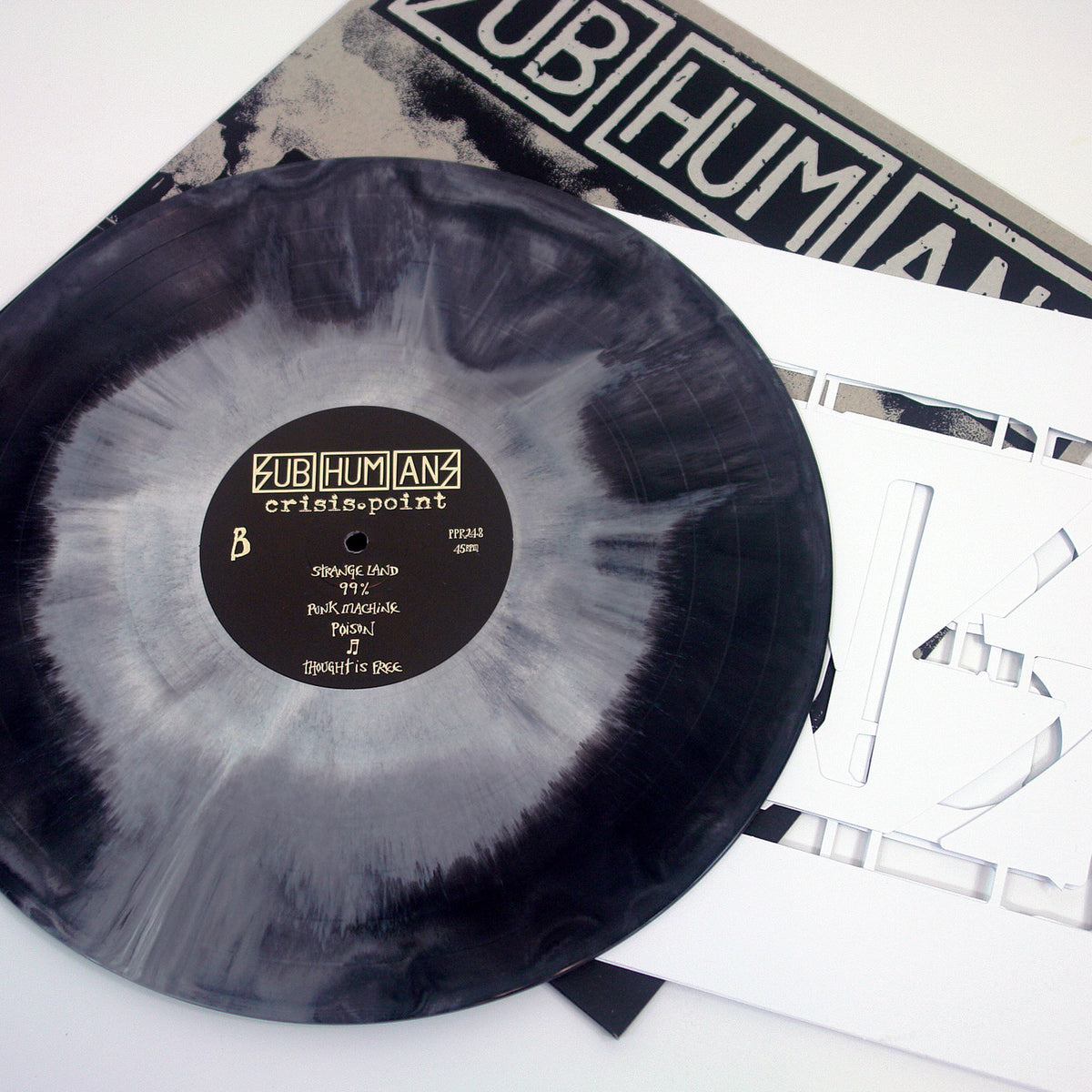 A marbled black and white vinyl record by Subhumans, titled Crisis Point, sits next to its album cover and a white insert featuring cut-out letters.