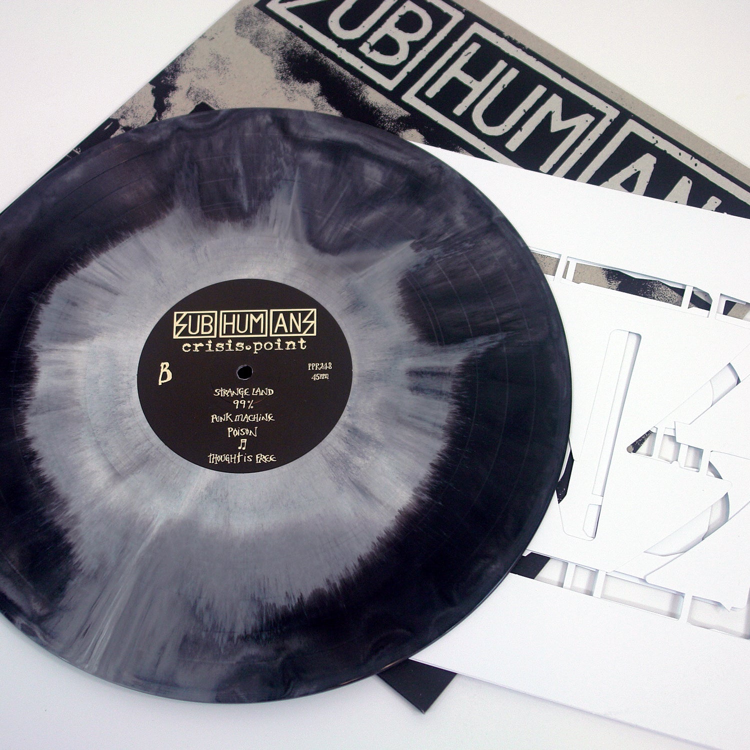 A marbled black and white vinyl record by Subhumans, titled Crisis Point, sits next to its album cover and a white insert featuring cut-out letters.